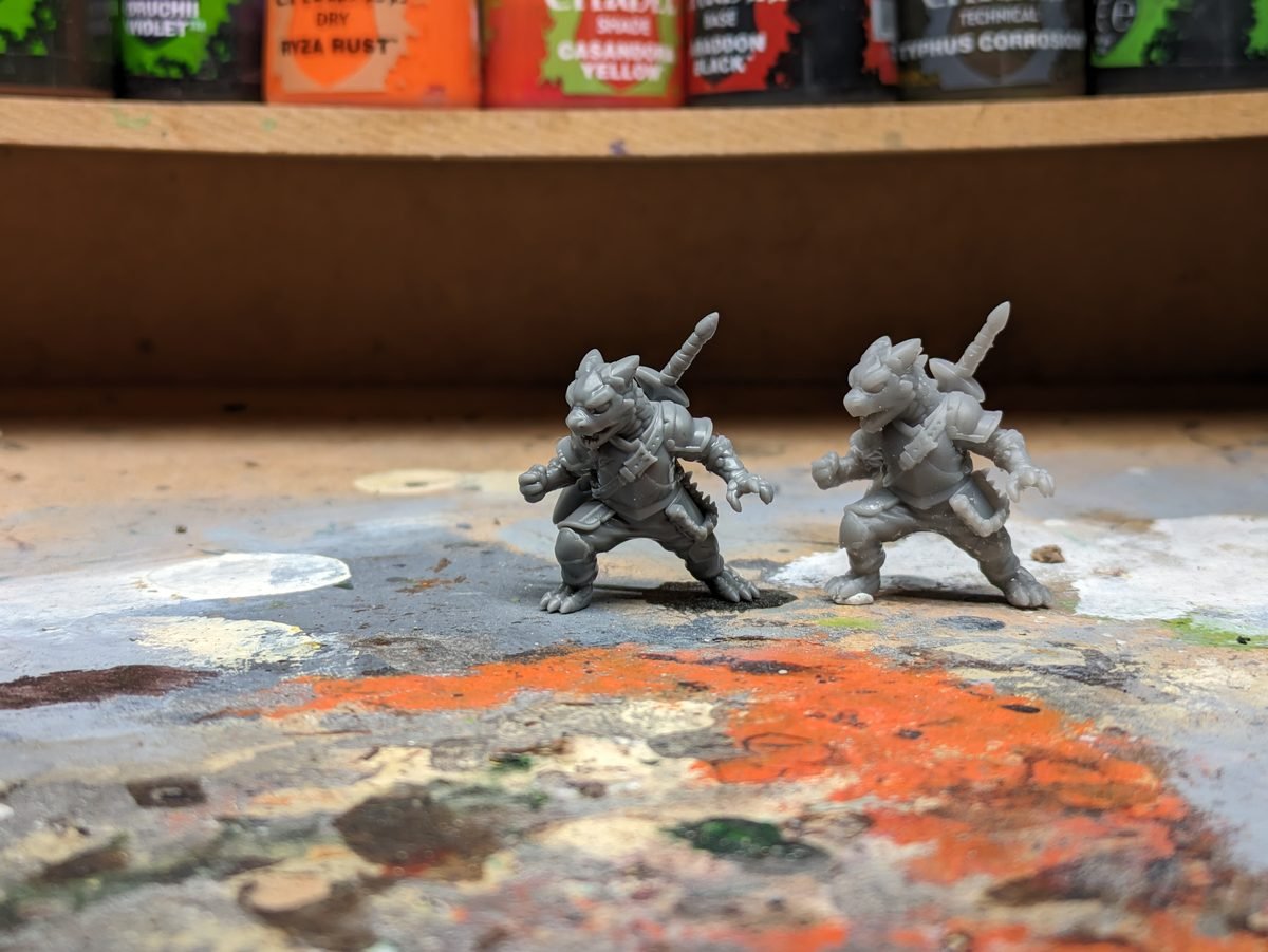 Two 3D printed resin miniatures fresh off the printer on a hobby desk